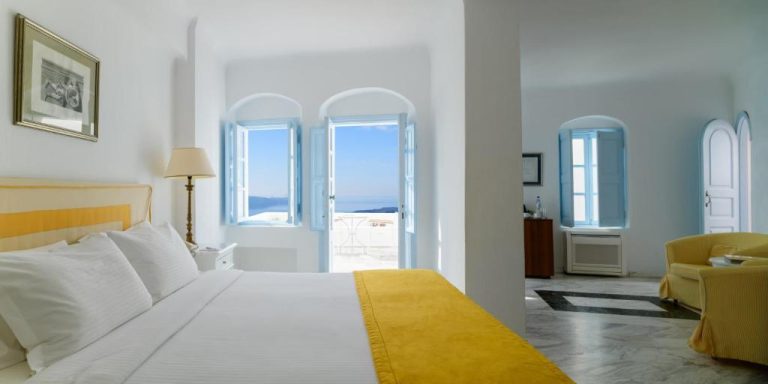 a bedroom with a bed and a chair and windows at Aigialos Luxury Traditional Settlement in Fira 768x384
