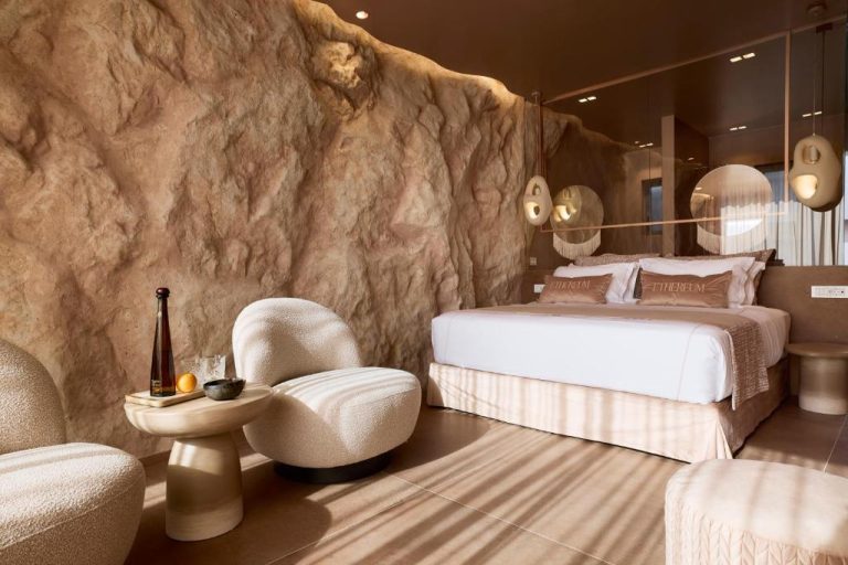 a bedroom with a bed and chairs and a wall at Ethereum Luxury Suites a member of Mykonos Highlights in Mikonos 768x512