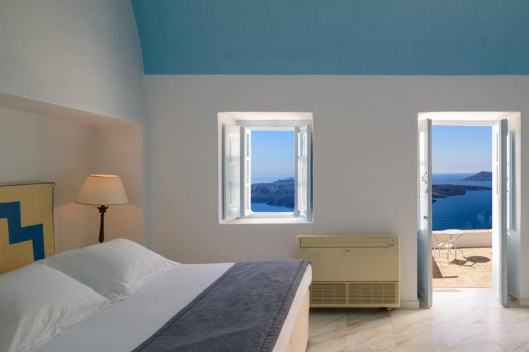 a bedroom with a bed and two windows at Aigialos Luxury Traditional Settlement in Fira 768x512