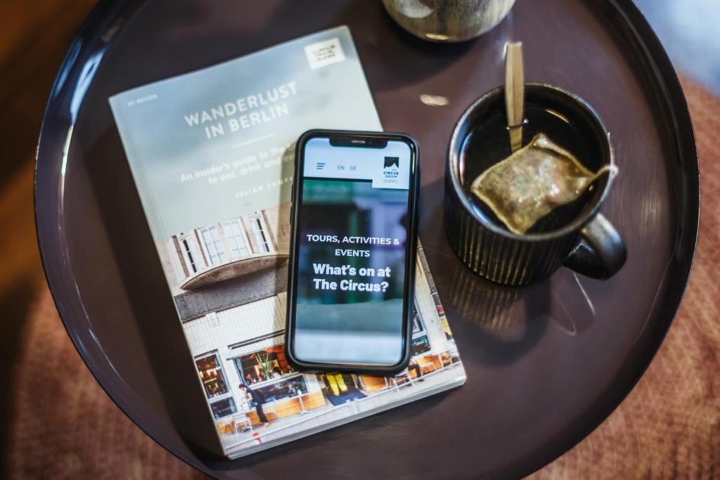 a cell phone on a table with a book and a cup of coffee at The Circus Apartments in Berlin