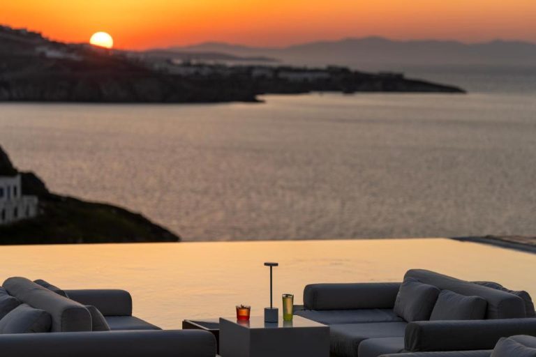 a living room with a view of the ocean at sunset at BillCoo Mykonos The Leading Hotels of the World in Mikonos 768x512