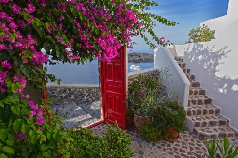 a red door in a white wall with flowers at Aigialos Luxury Traditional Settlement in Fira 768x512