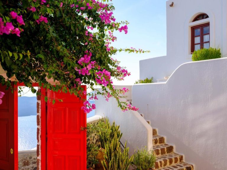 a red door on a white wall with pink flowers at Aigialos Luxury Traditional Settlement in Fira 768x576