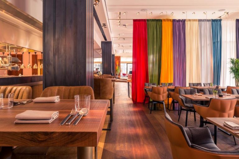 a restaurant with wooden tables and chairs and colorful curtains at Orania.Berlin in Berlin 768x512