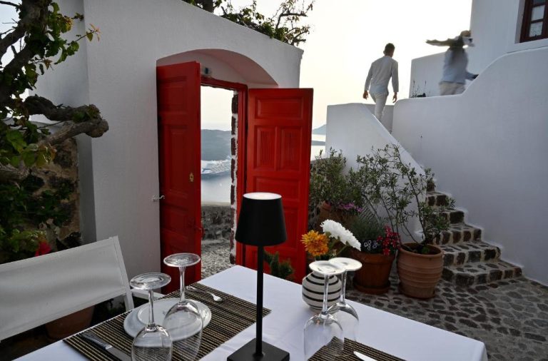 a table with a red door and a man walking down the stairs at Aigialos Luxury Traditional Settlement in Fira 768x506