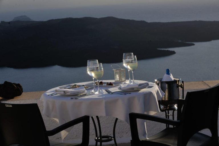 a table with glasses of white wine on it at Aigialos Luxury Traditional Settlement in Fira 768x512