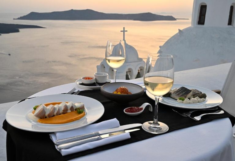 a table with two plates of food and glasses of wine at Aigialos Luxury Traditional Settlement in Fira 768x524