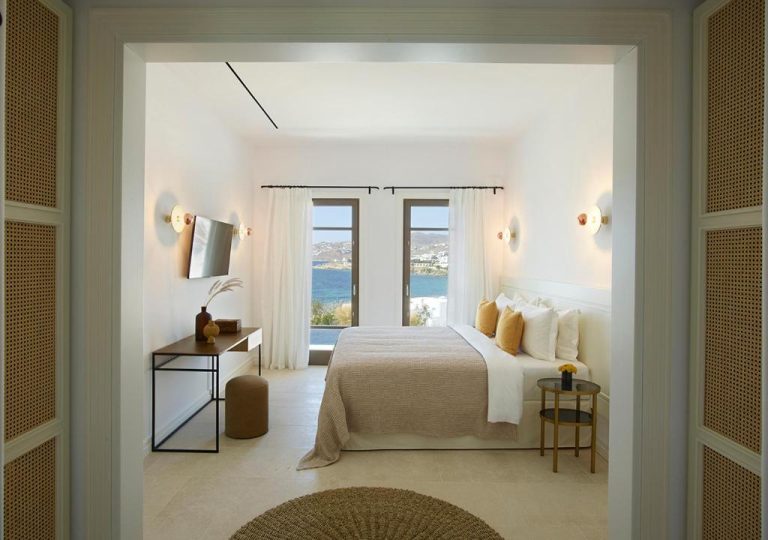 a white bedroom with a bed and a window at Bonzoe Suites Villas in Mikonos 768x540