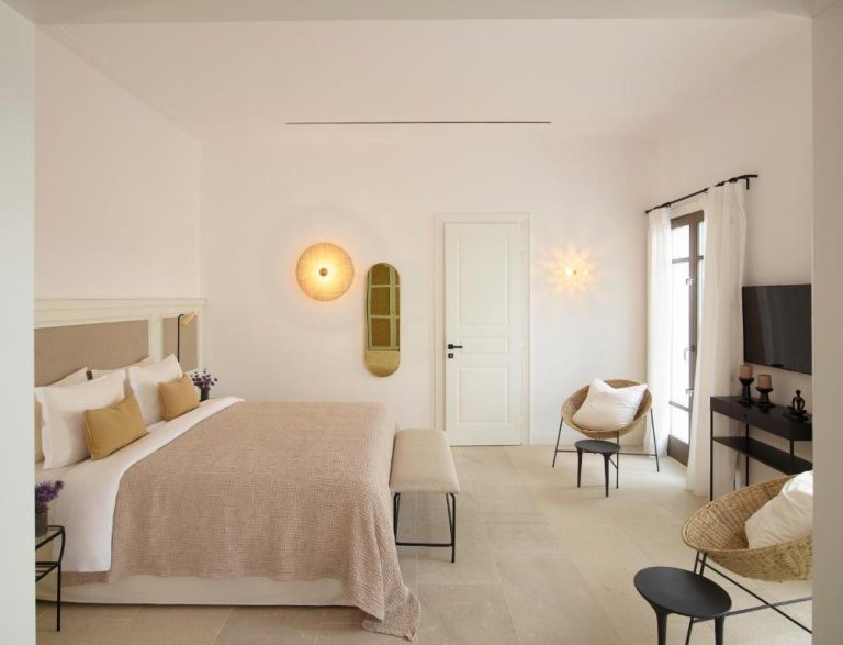 a white bedroom with a large bed and a chair at Bonzoe Suites Villas in Mikonos 768x587