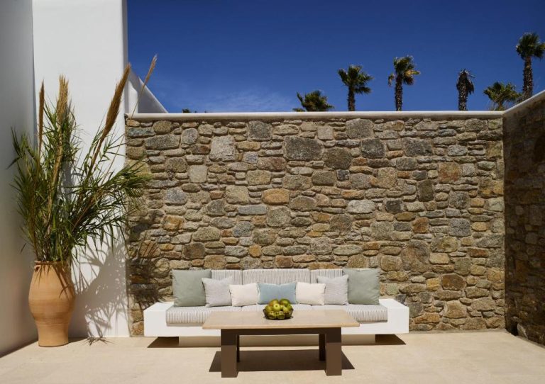 a white couch in front of a stone wall at Bonzoe Suites Villas in Mikonos 768x542