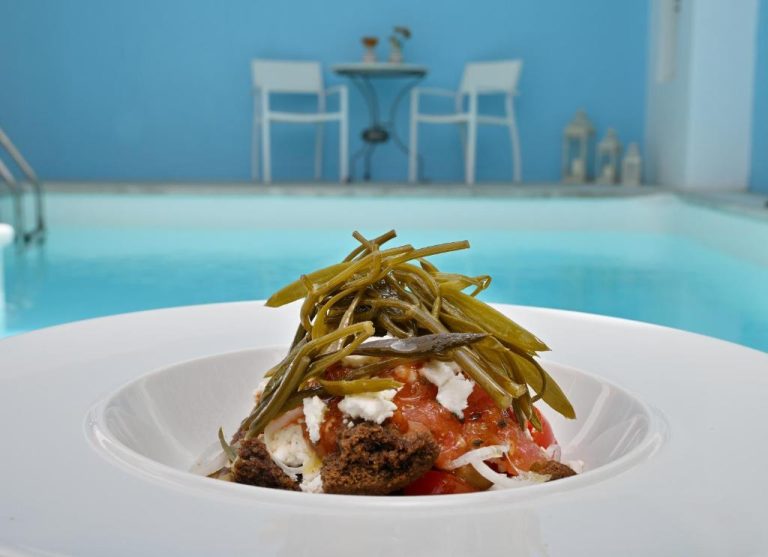 a white plate with a dish of food on a table at Aigialos Luxury Traditional Settlement in Fira 768x557