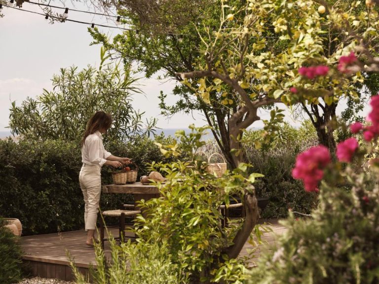 a woman standing on a wooden deck in a garden at Boheme Mykonos Town Small Luxury Hotels of the World in Mikonos 768x576