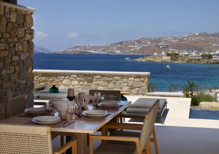 a wooden table and chairs with a view of the ocean at Bonzoe Suites Villas in Mikonos 768x540