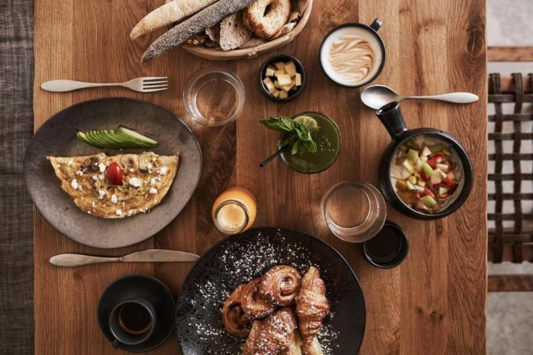 a wooden table with plates of food on it at Amyth of Mykonos Agios Stefanos in Agios Stefanos 768x512